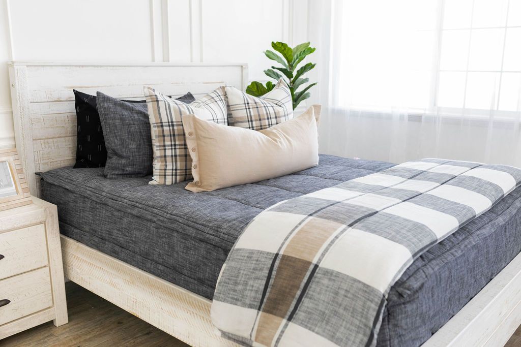 Dark gray charcoal zipper bedding with matching sham and black pillow cases. Decorated with cream plaid pillows, cream lumbar pillow, and cream and gray plaid blanket