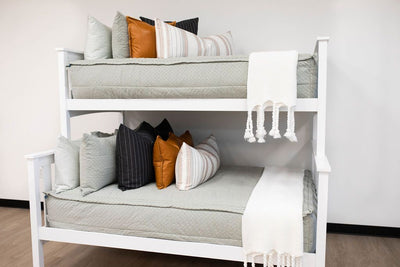 Green zipper bedding on bunk beds styled with green, brown leather, cream and black pillows. White throw blanket at foot of beds