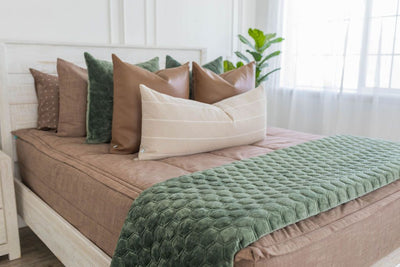 Brown zipper bedding with brown pillow cases and shams. Decorated with green and brown leather pillow. Cream lumbar pillow and green blanket