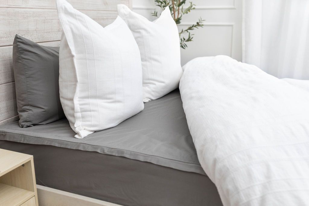 A side view of a bed made with a gray zipper sheet set and a textured white zipper duvet and matching white and gray pillows. 
