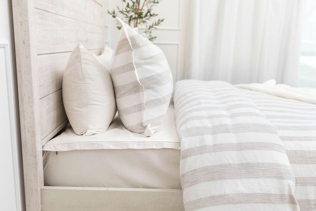 A side view of a bed made with a white zipper sheet set and a white and tan textured zipper duvet and matching pillows.