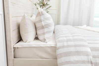 A side view of a bed made with a white zipper sheet set and a white and tan textured zipper duvet and matching pillows.