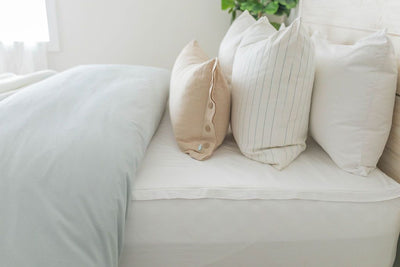 A side view of a bed made with a white zipper sheet set and a blue two-toned zipper duvet and matching neutral pillows.